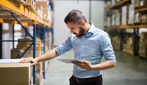 Certificat Supply Chain e-commerce, formation continue de Dauphine Executive Education (visuel présentation) Un professionnelle de la supply chain travaille avec une tablette dans un entrepôt rempli de cartons. Programmes de formation continue en Supply Chain et e-commerce de Dauphine Executive Education