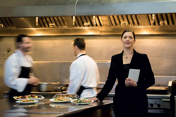 Femme professionnelle de l'hotellerie et restauration travaillant dans une cuisine de restaurant avec deux cuisiniers. Programme de formation continue en management hotelier et restauration de Dauphine Executive Education et Le Cordon Bleu